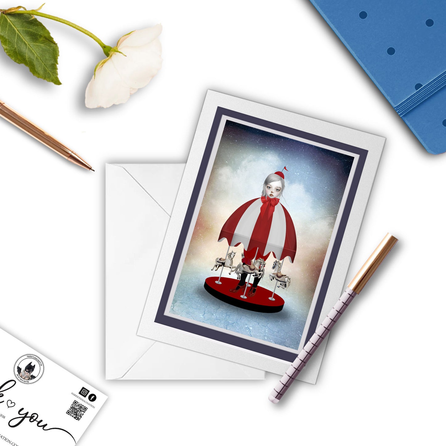 Carousel Art Greeting Card with pen and other stationary items arranged around it.