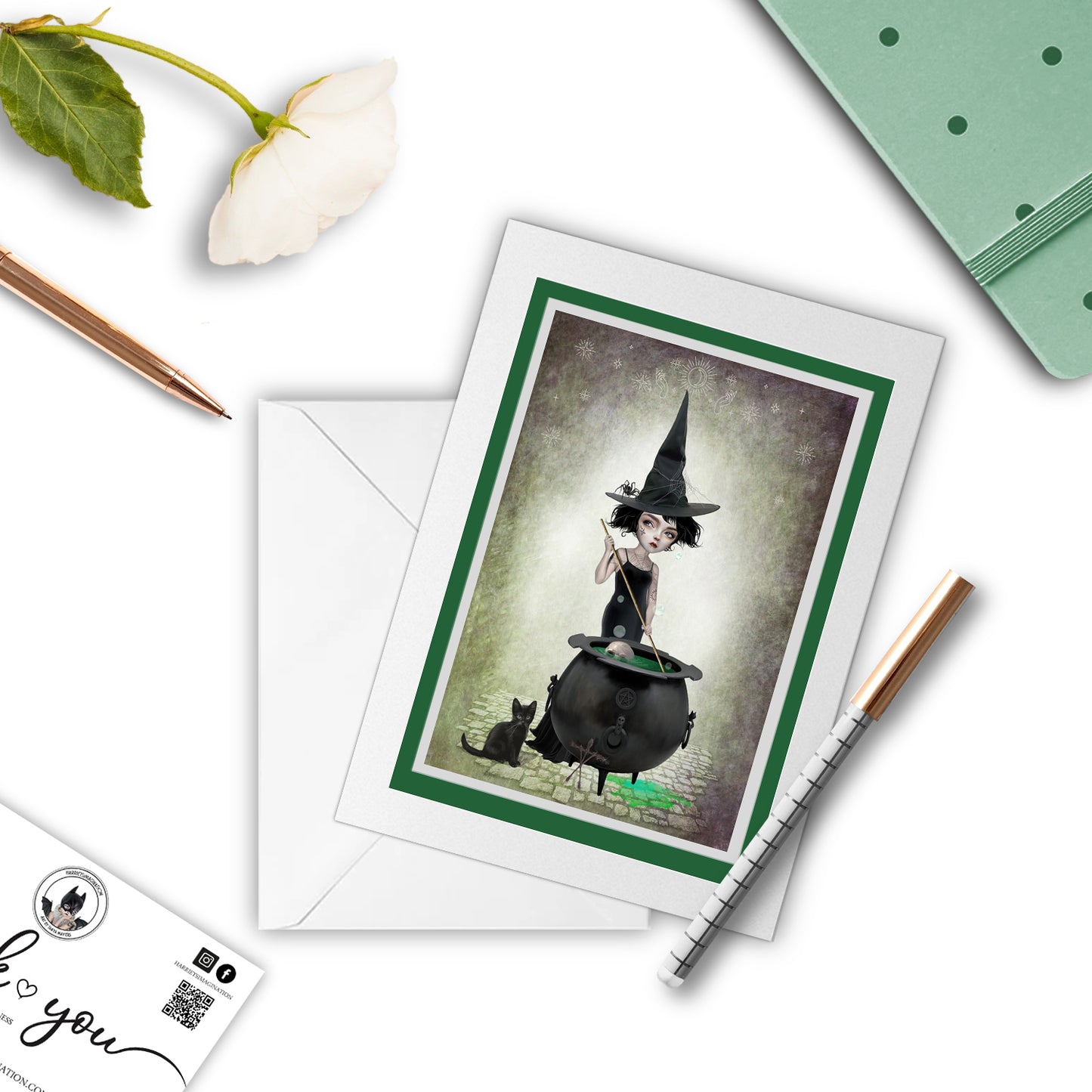 Witch and caulron card. with a pen and other stationary items arranged around it.