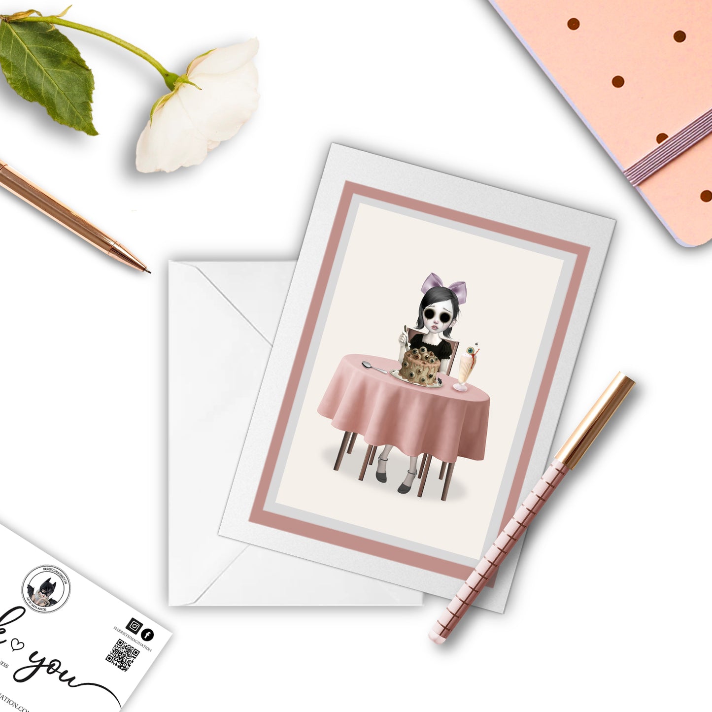 Surreal greeting card with notebook and pen – eyeball cake design flatlay.