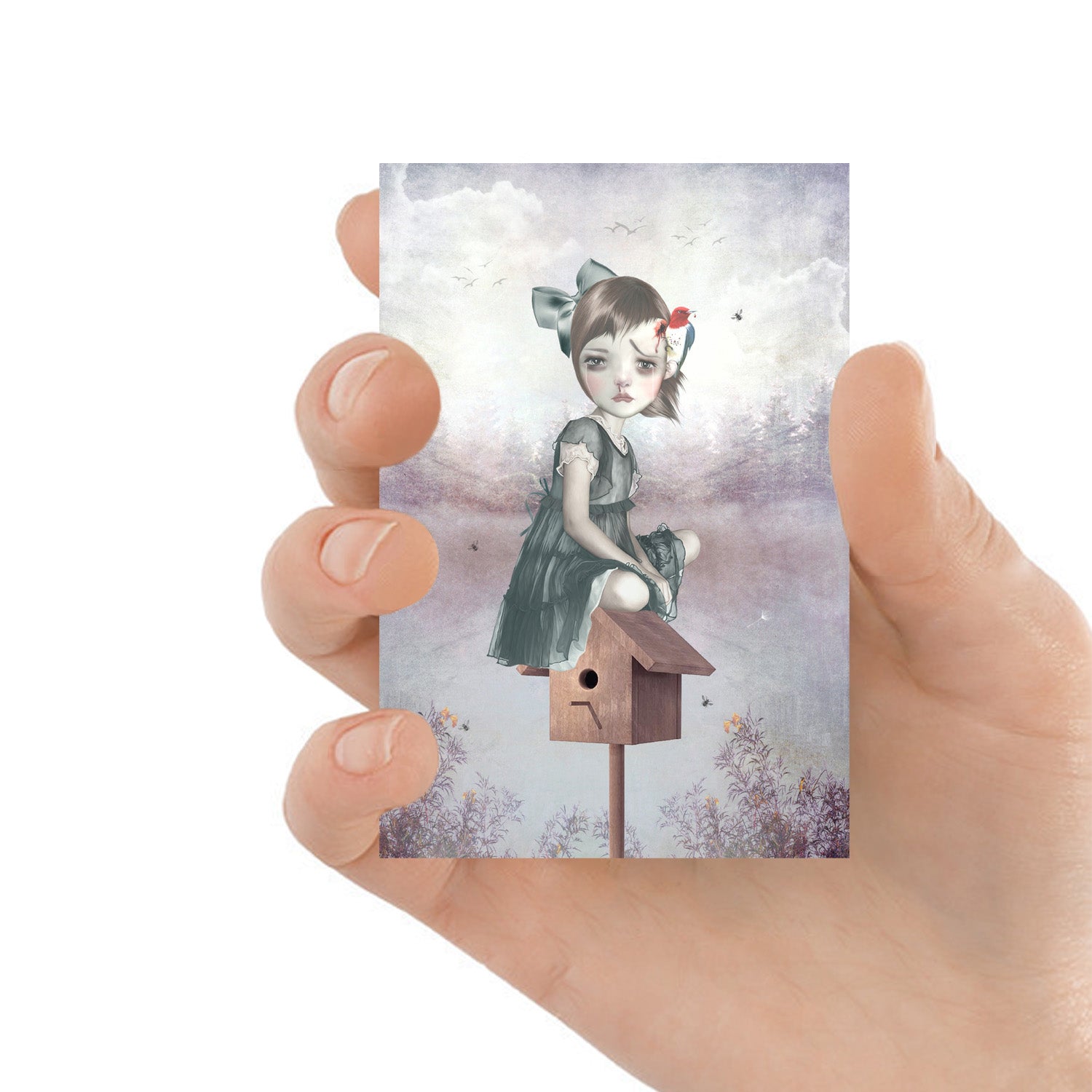 ACEO card featuring a surreal art print of a girl sitting on a birdhouse with a woodpecker pecking her head, held in hand for a personal, close-up view.