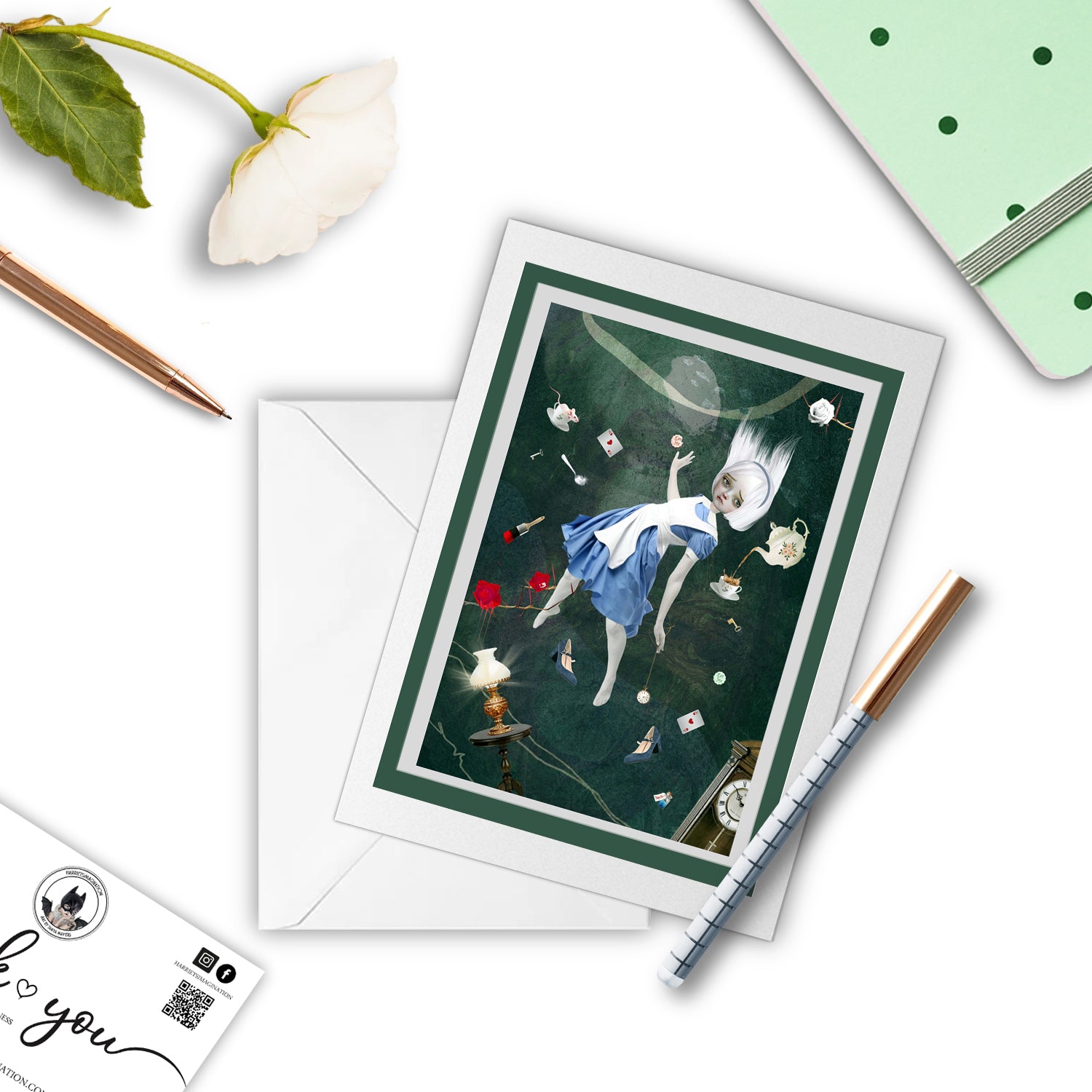Mockup of Alice in Wonderland-themed greeting card featuring Alice falling down the rabbit hole, with a pen and other stationery items arranged around it.