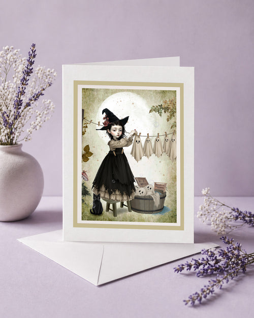 Blank frameable art greeting card featuring a gothic witch girl hanging sheet ghosts on a clothesline next to a white envelope