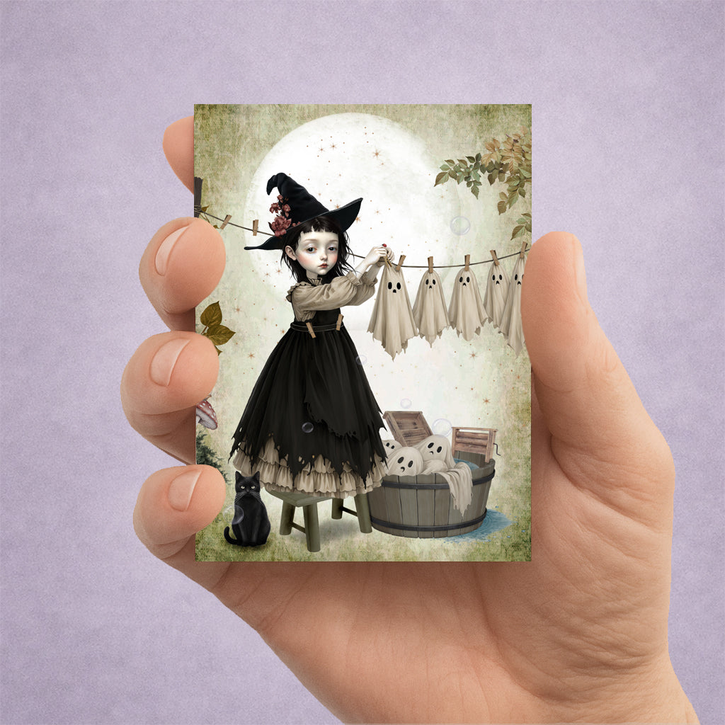 Miniature 2.5x3.5 ACEO art trading card of a gothic witch girl hanging sheet ghosts on a clothesline, held in hand for display