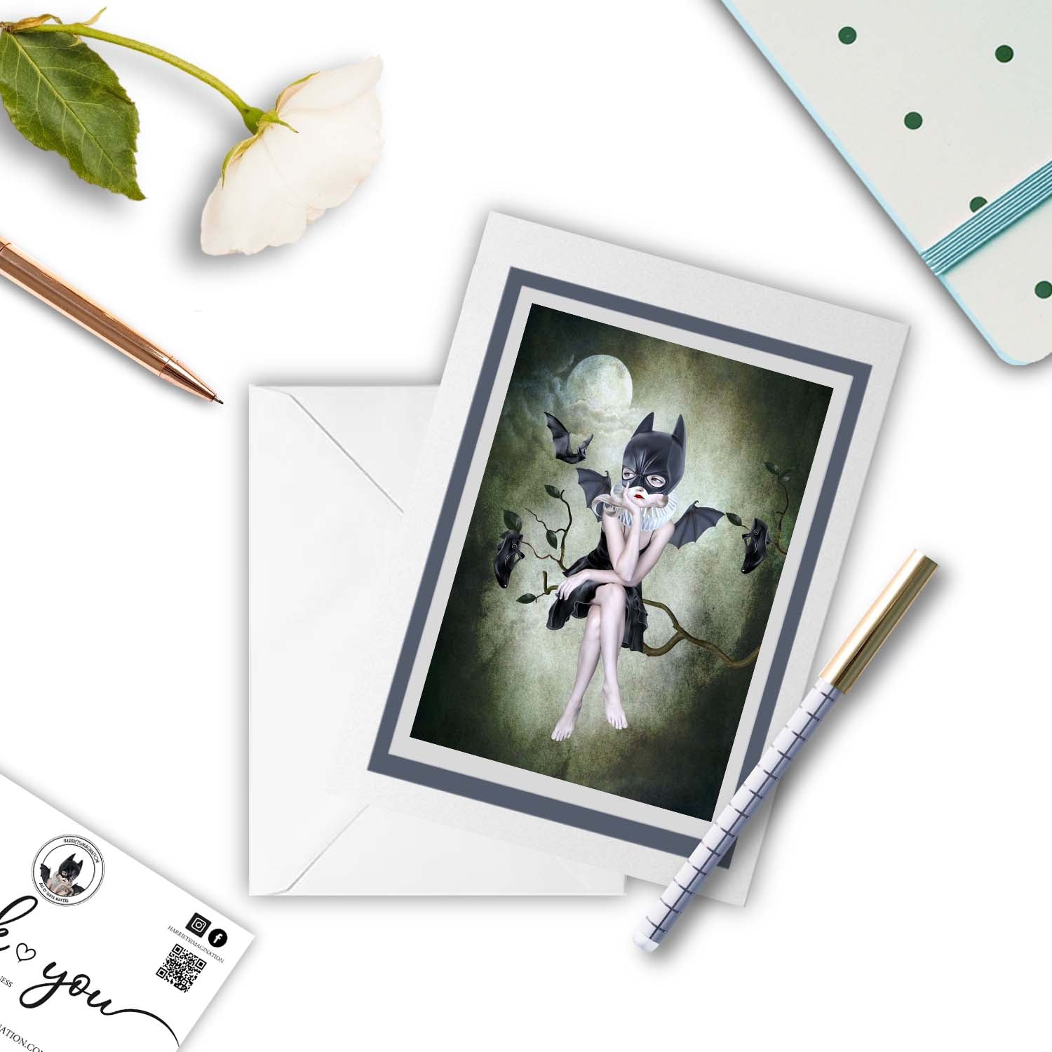 Bat girl and bats moonlighting art greeting card , with a pen and other stationary items arraged around it.