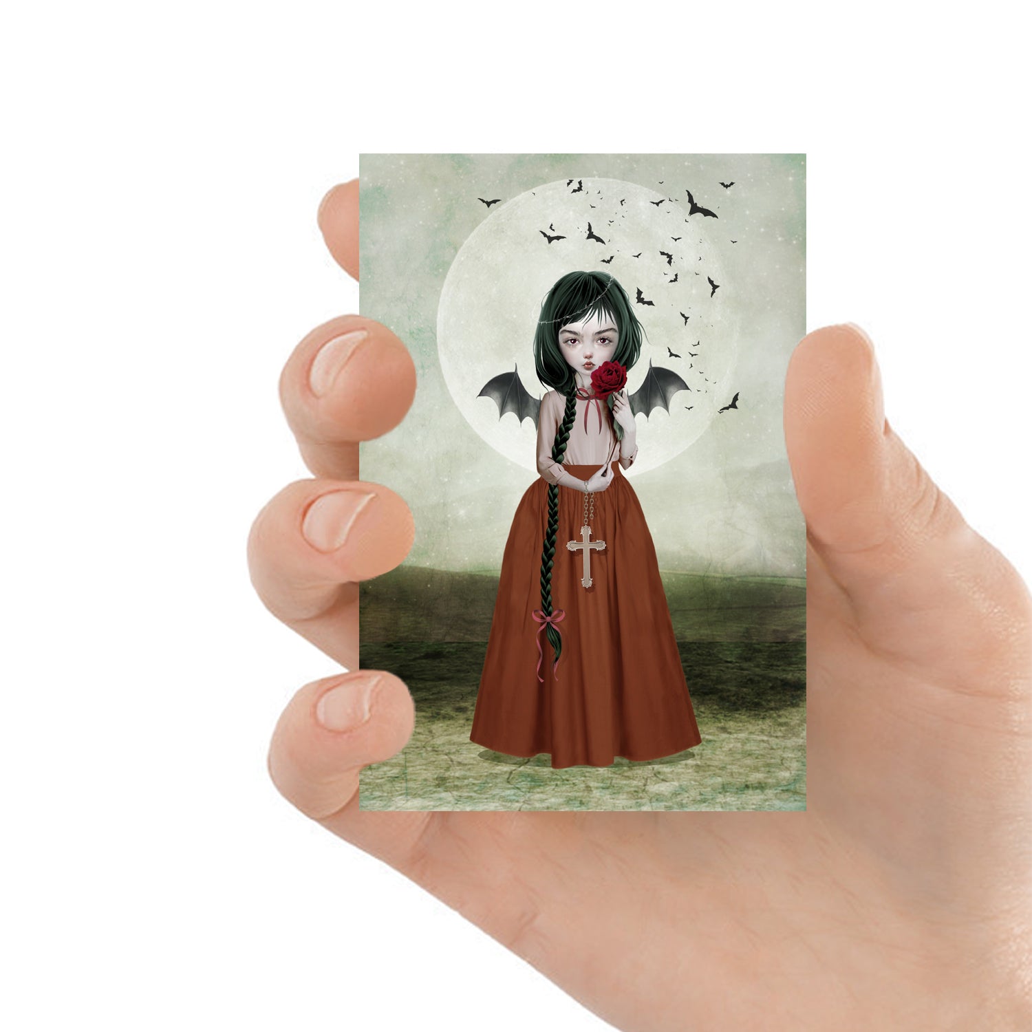 ACEO-sized Batgirl artwork held in hand, showcasing its compact size. Dark gothic fantasy art featuring a crucifix under the moonlight, perfect for collectors.