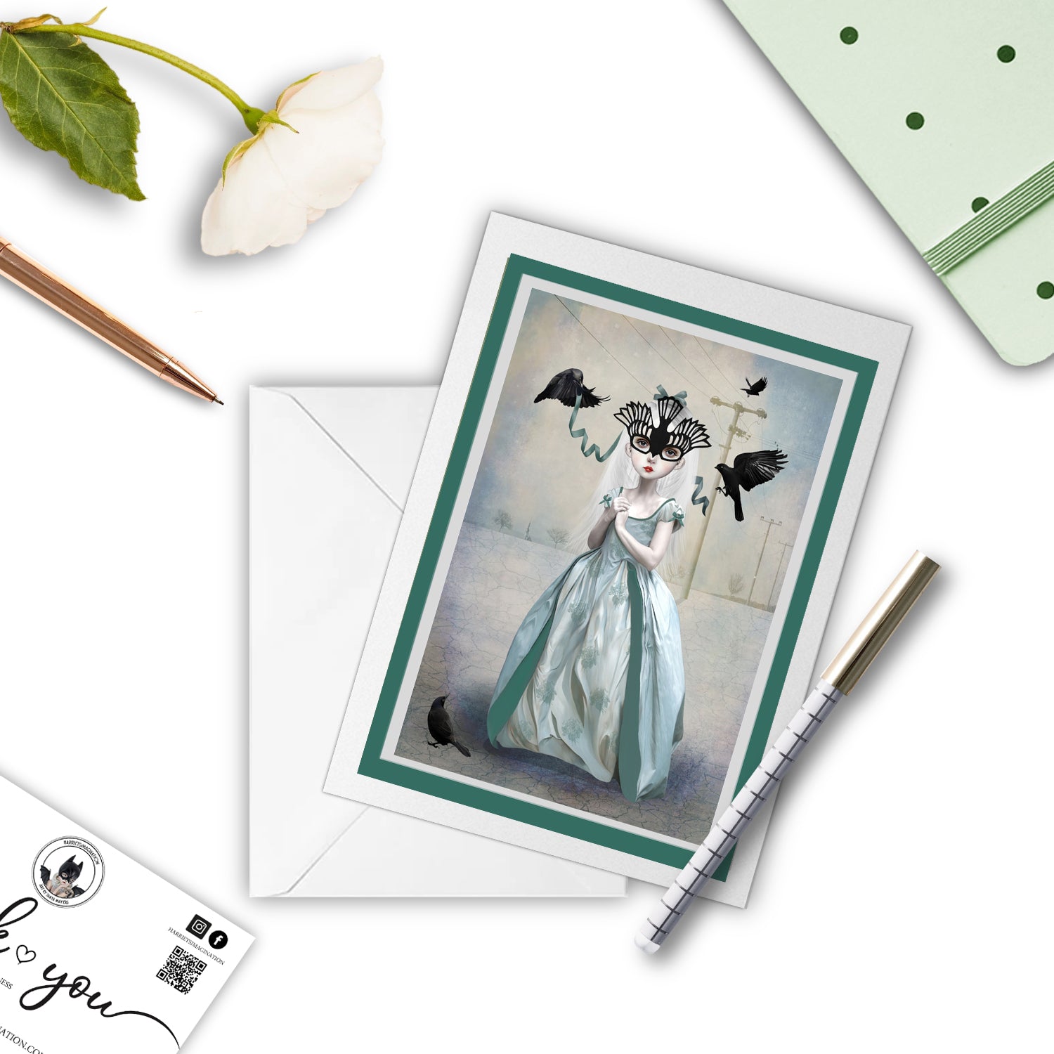 Bird Girl And Blackbirds Art Greeting with a pen and other stationary items arranged around it.