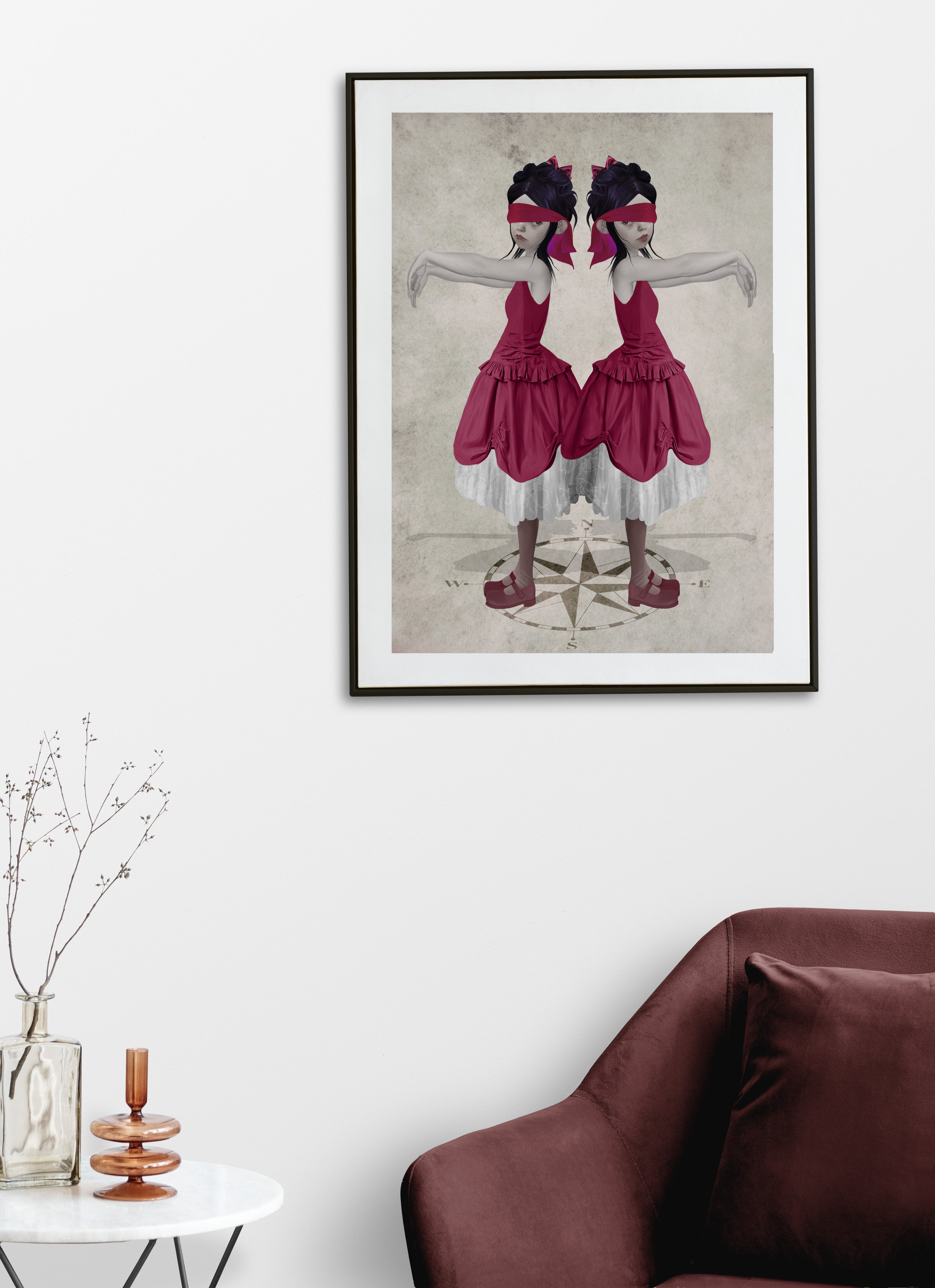 Framed artwork of two twin sisters in red dresses and compass on a white wall above a brown sofa.