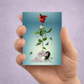 Hand holding an ACEO card with a surreal design of an anatomical heart growing with a plant from a sad girls spine.