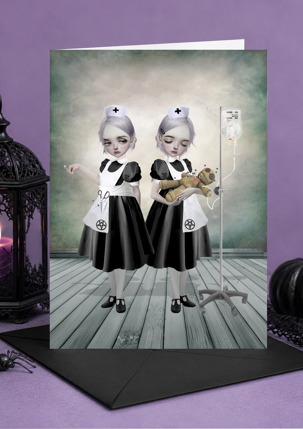 Halloween card featuring gothic twin nurses in black dresses and pentagram aprons tending to a voodoo doll with an IV drip.