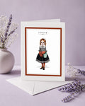 Cancer zodiac birthday card featuring an illustration of a red-haired maiden in a nautical sailor dress with crab claw hands and a beach bucket.