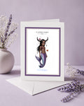 Capricorn zodiac birthday card featuring an illustration of a mermaid with dark skin, goat horns draped in pearls, and a iridescent purple fish tail.