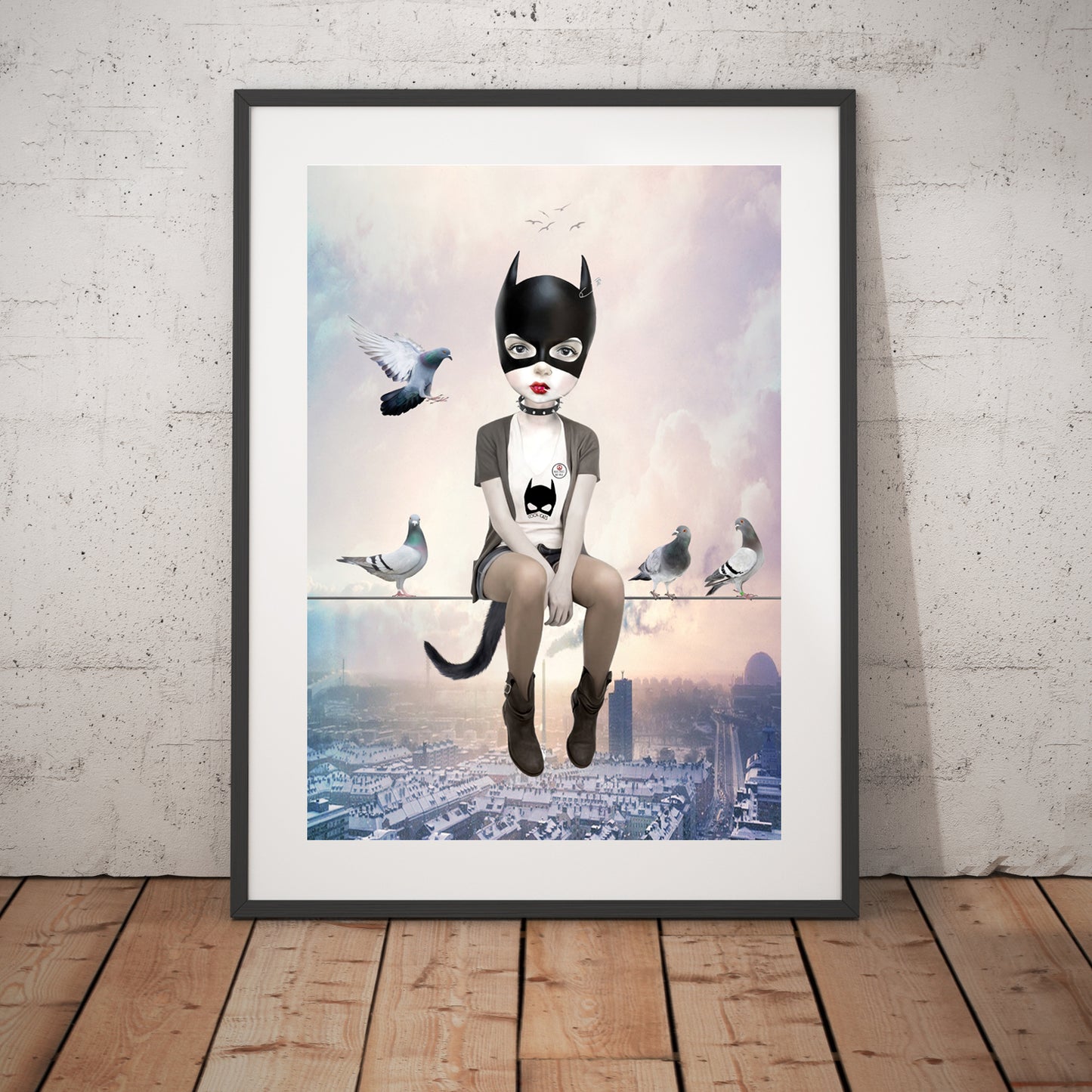 Cat Girl and pigeons art print in a black frame, standing against a white wall.