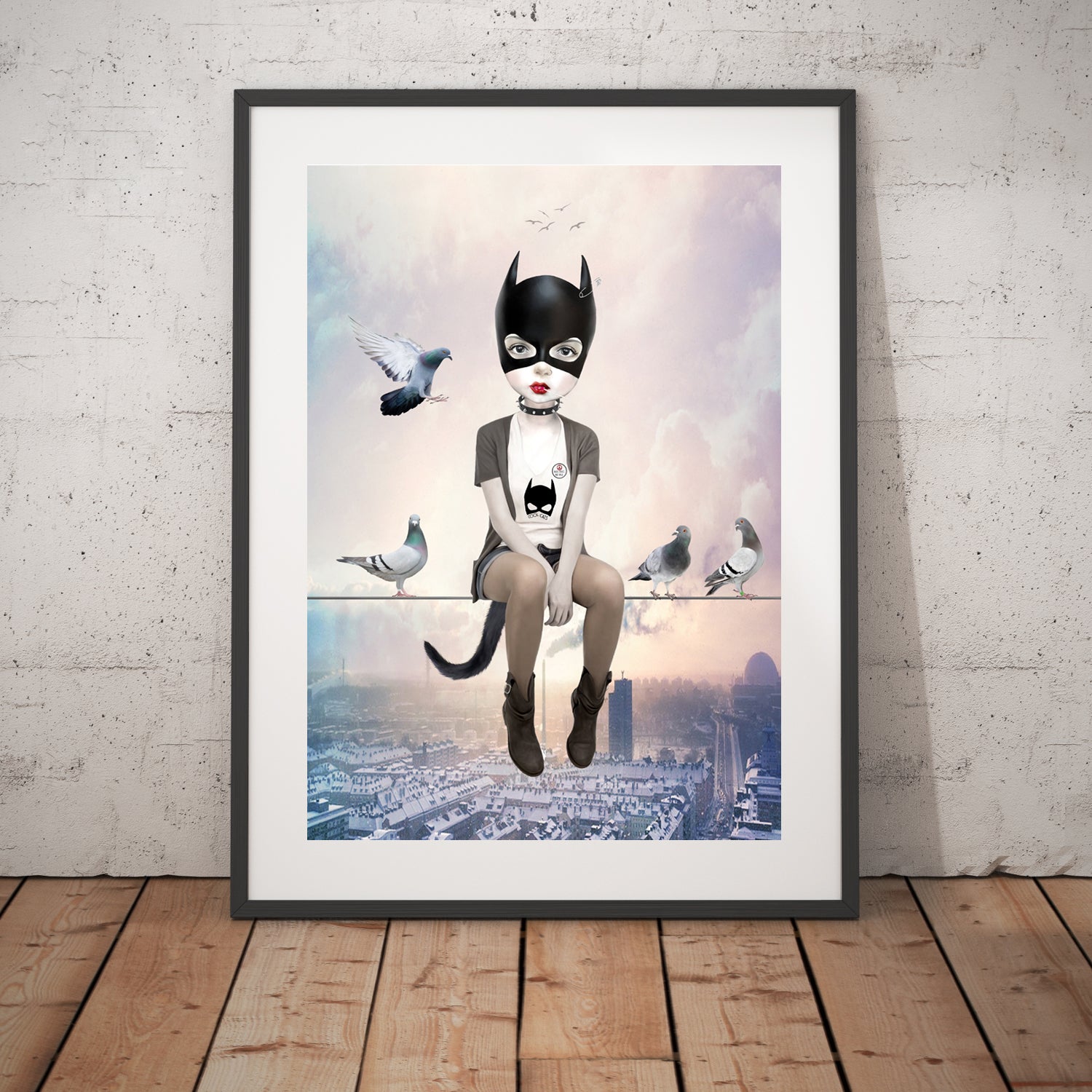 Cat Girl and pigeons art print in a black frame, standing against a white wall.