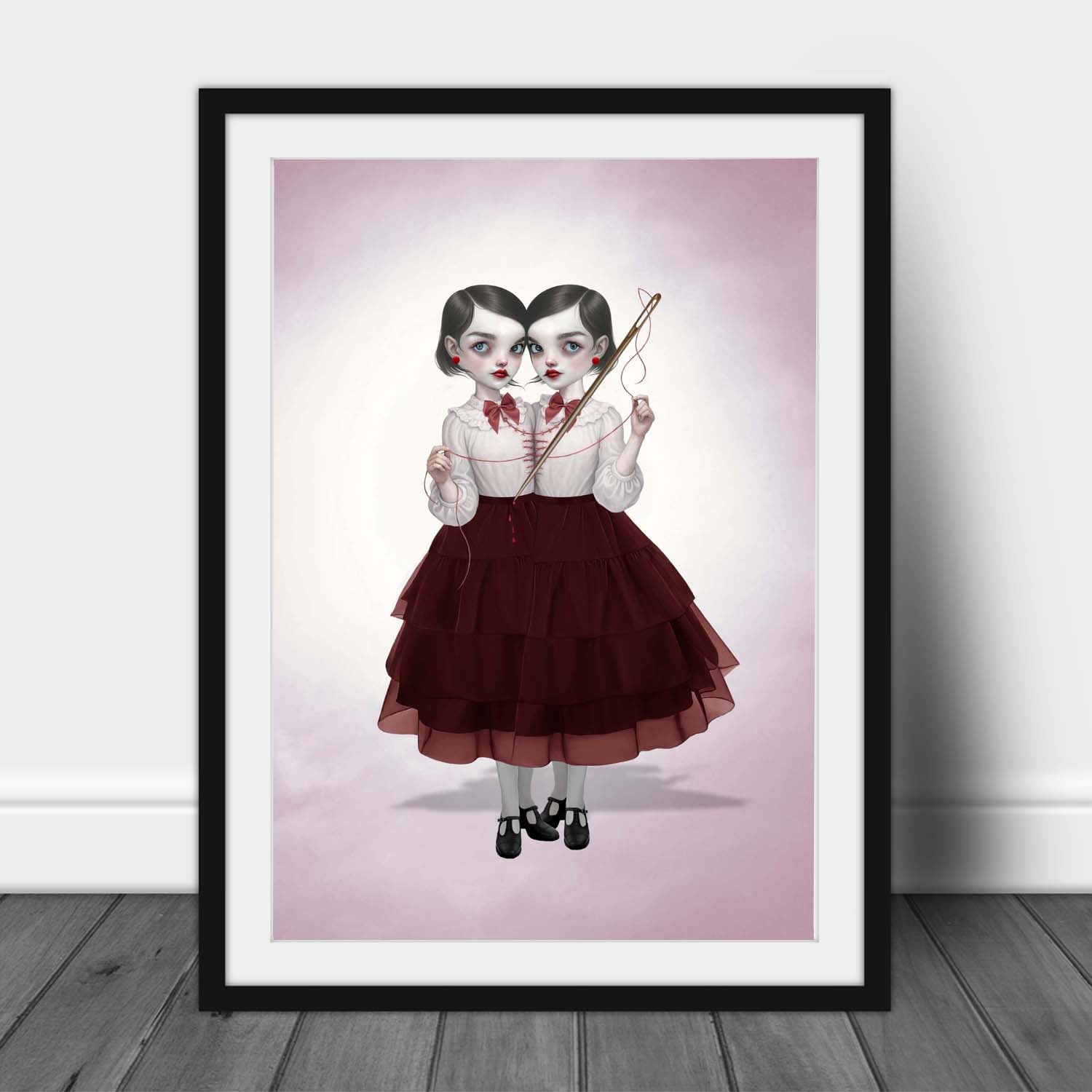 dark pop surrealism art print in an A3 frame mockup. This gothic illustration features conjoined twin girls with a needle and thread.
