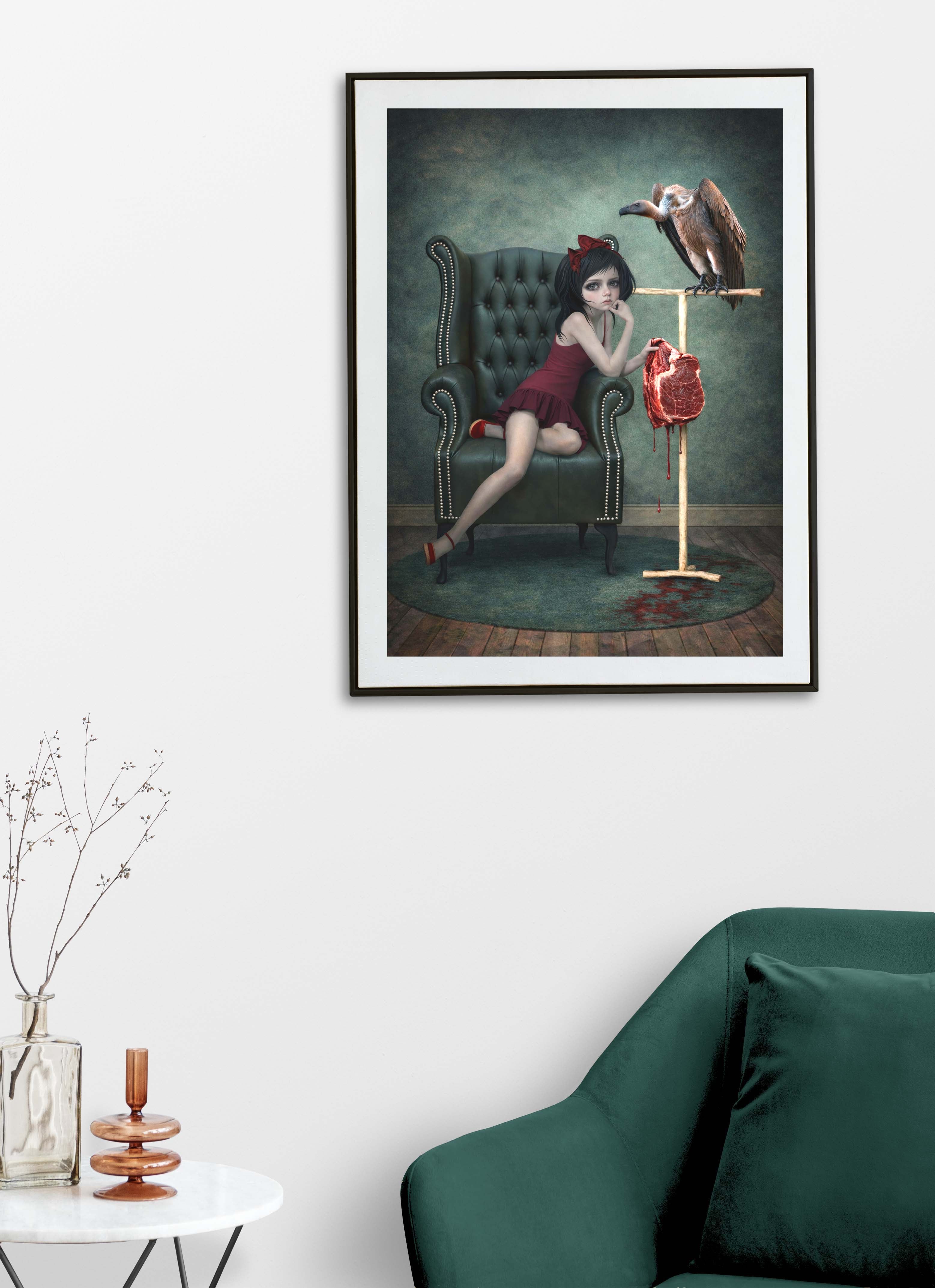 Framed artwork of a girl in a red dress offering her pet vulture raw meat., displayed in a room with a green sofa and decorative items.