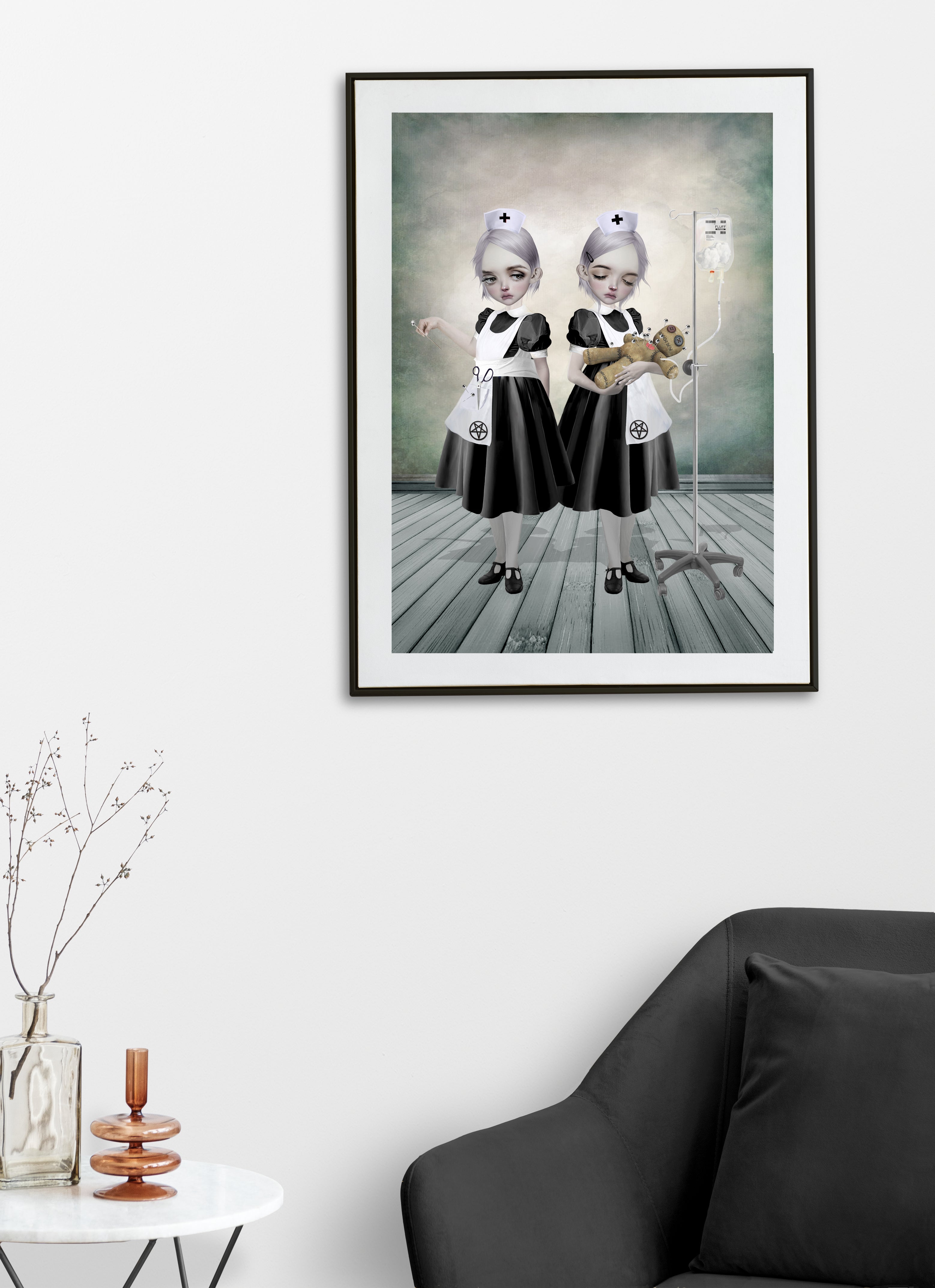 Framed artwork of two creepy cute nurses and voodoo doll on a white wall above a black sofa.