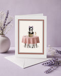 Greeting card with an eyeless girl at a table with eyeball cake on a purple background.