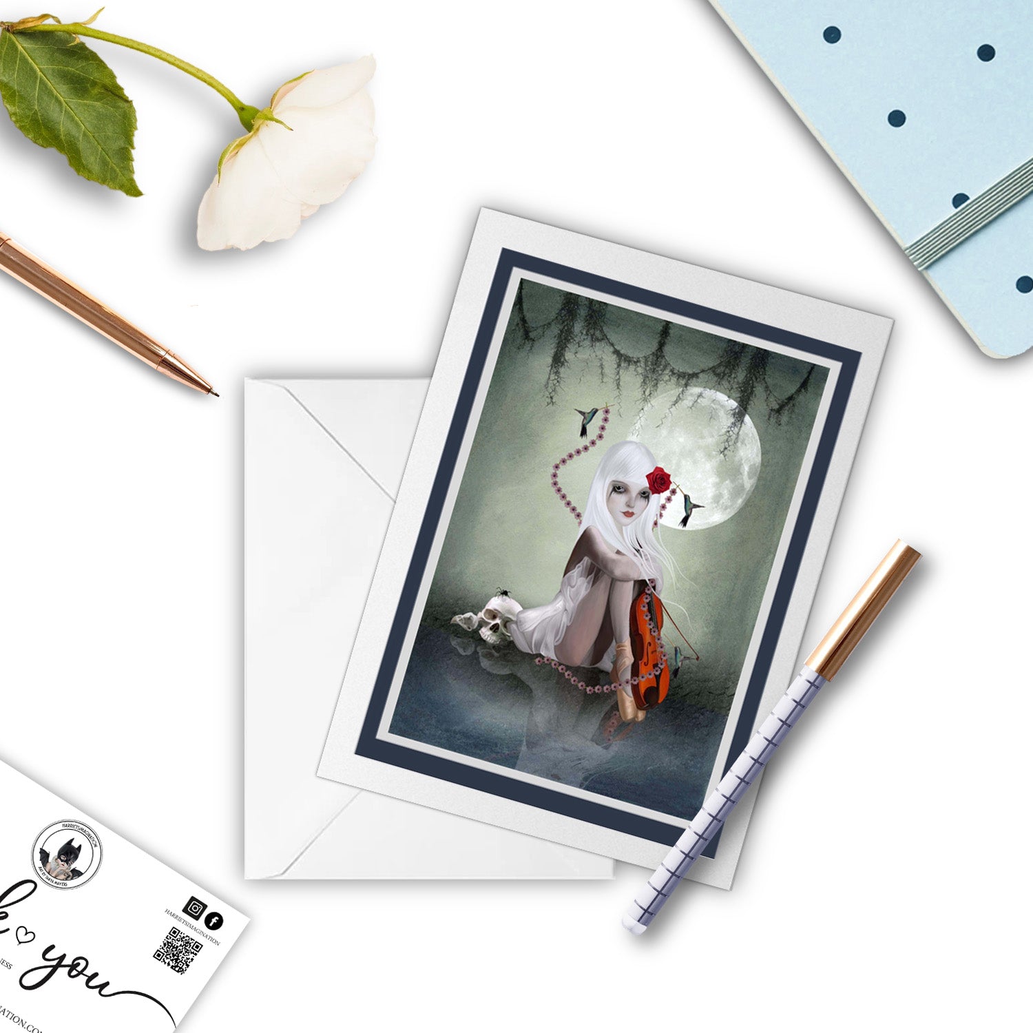 Dark fantasy greeting card featuring a girl with a skull, placed beside a pen and notebook. 