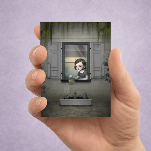 Creepy cute miniature print of a gothic girl watering graves, shown held in a hand.