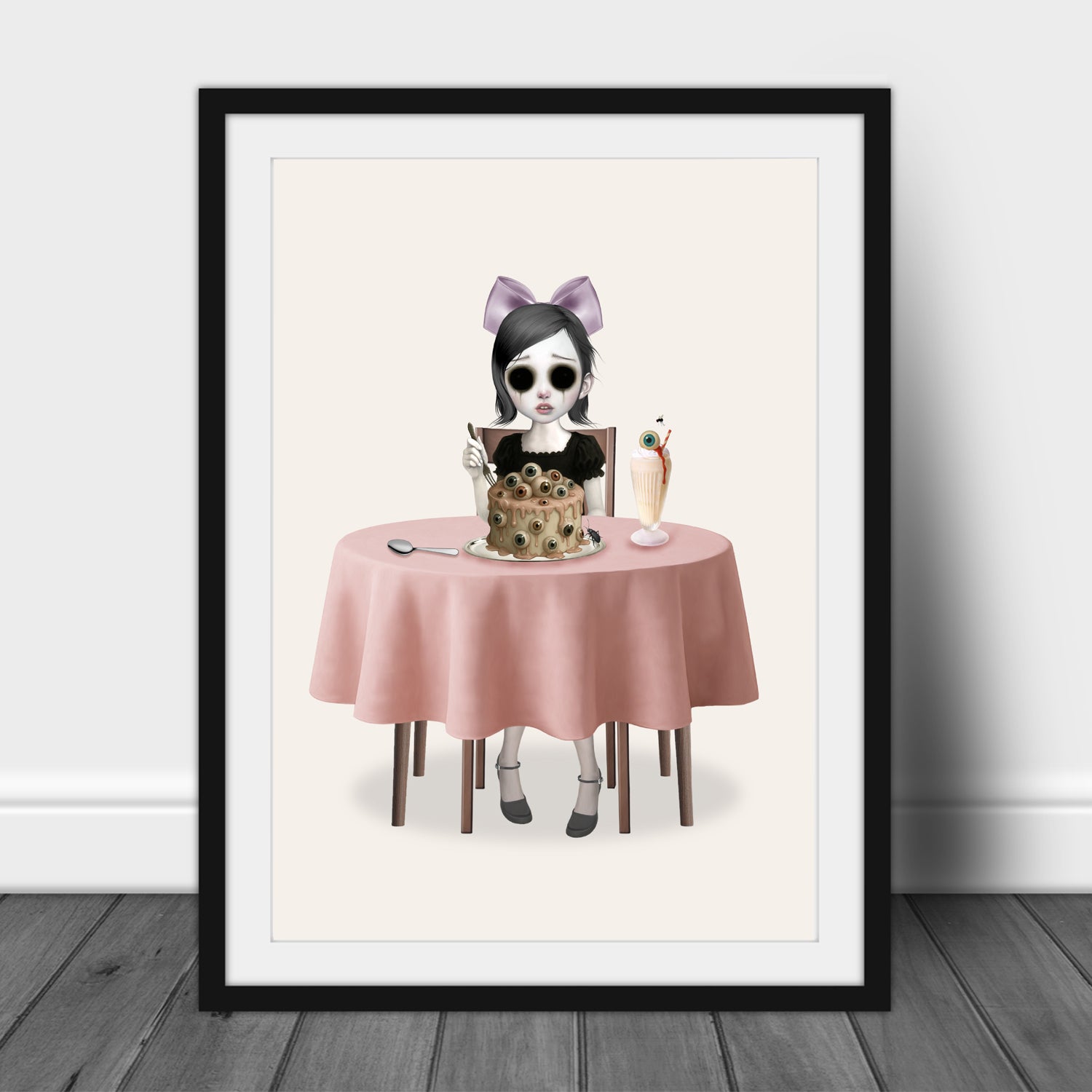 A Sight for Sore Eyes art print in a black frame leaning against a white wall, highlighting the creepy-cute aesthetic and soft pink color palette.