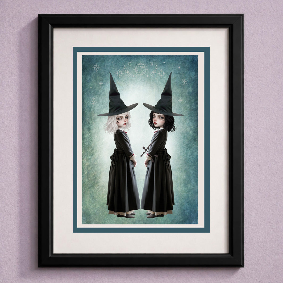 Framed  gothic art greeting card featuring twin witch sisters in black pointed hats standing back to back against a celestial teal background.