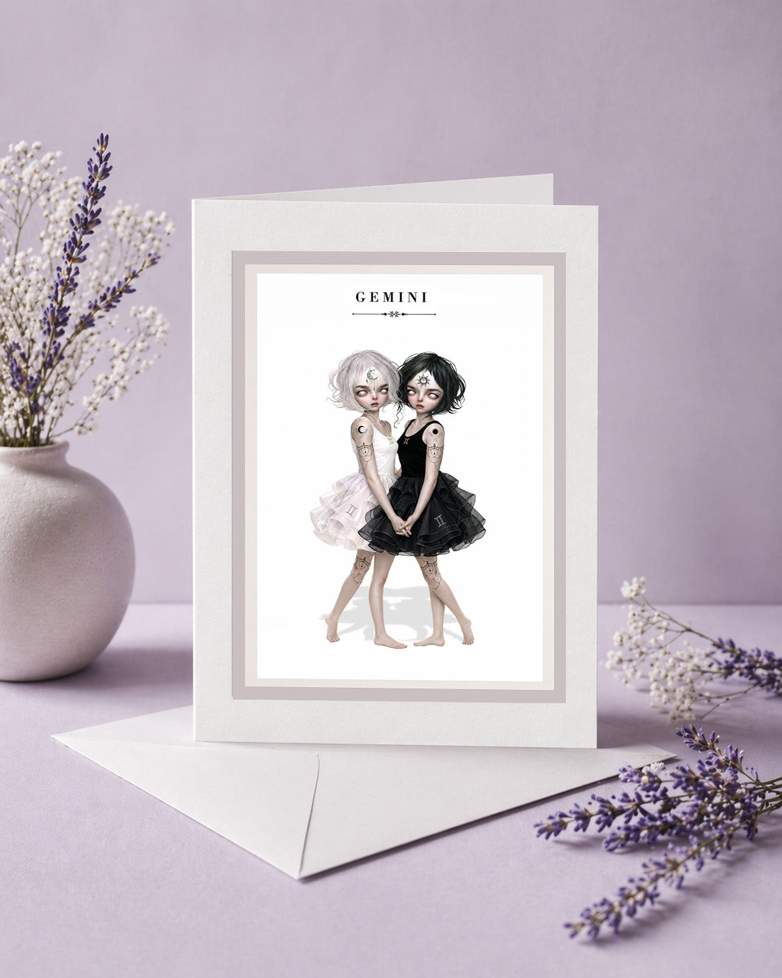Gemini zodiac birthday card featuring an illustration of twin maidens holding hands—one with white hair in a light dress and one with black hair in a dark dress.