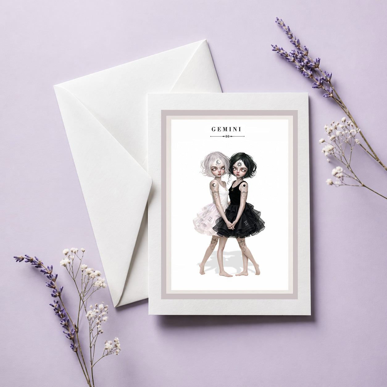 Gemini zodiac birthday card with envelope featuring an illustration of twin maidens holding hands—one with white hair in a light dress and one with black hair in a dark dress.