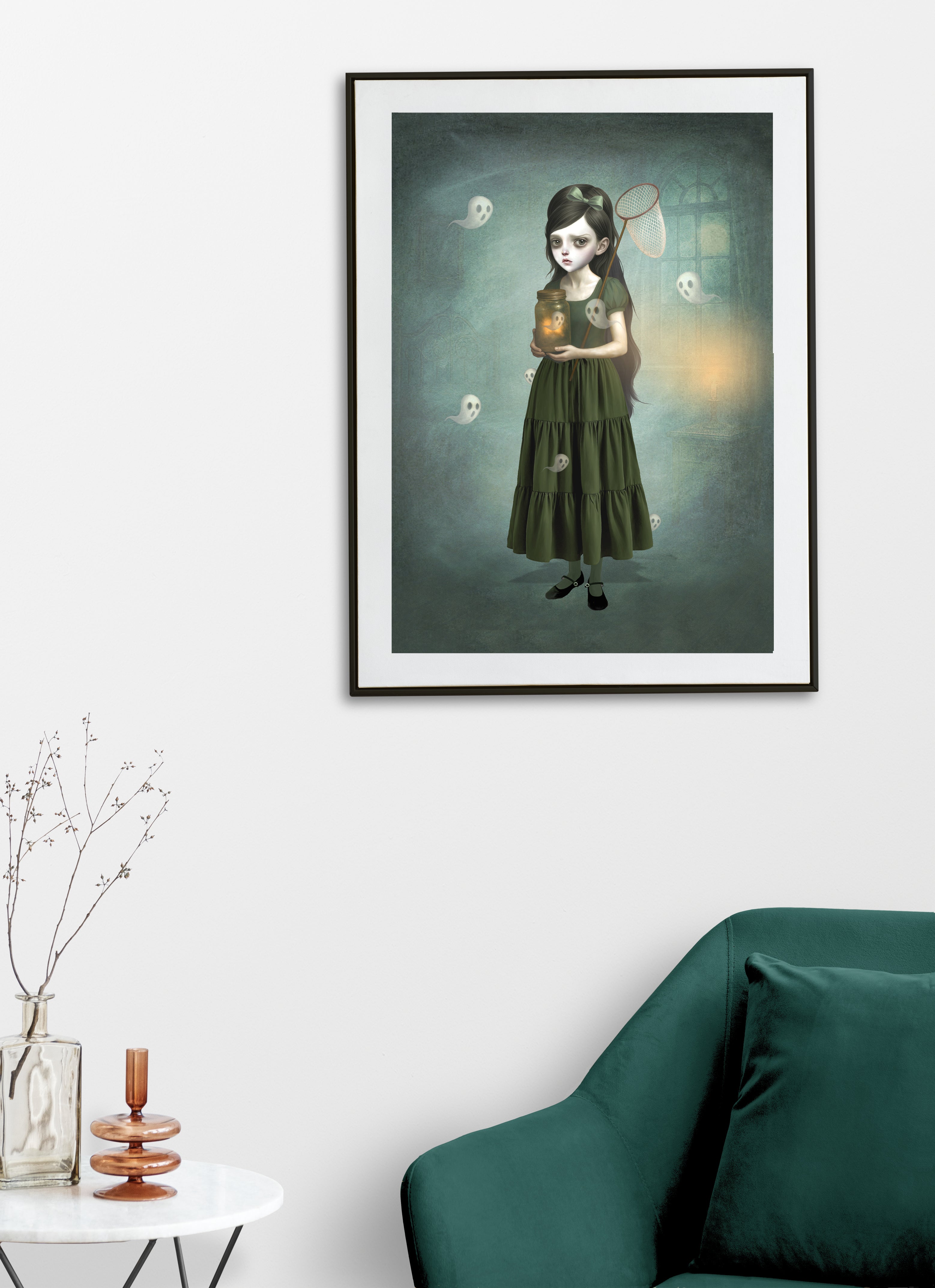 Framed artwork of a girl with a green dress catching ghosts hanging on a white wall above a green sofa.