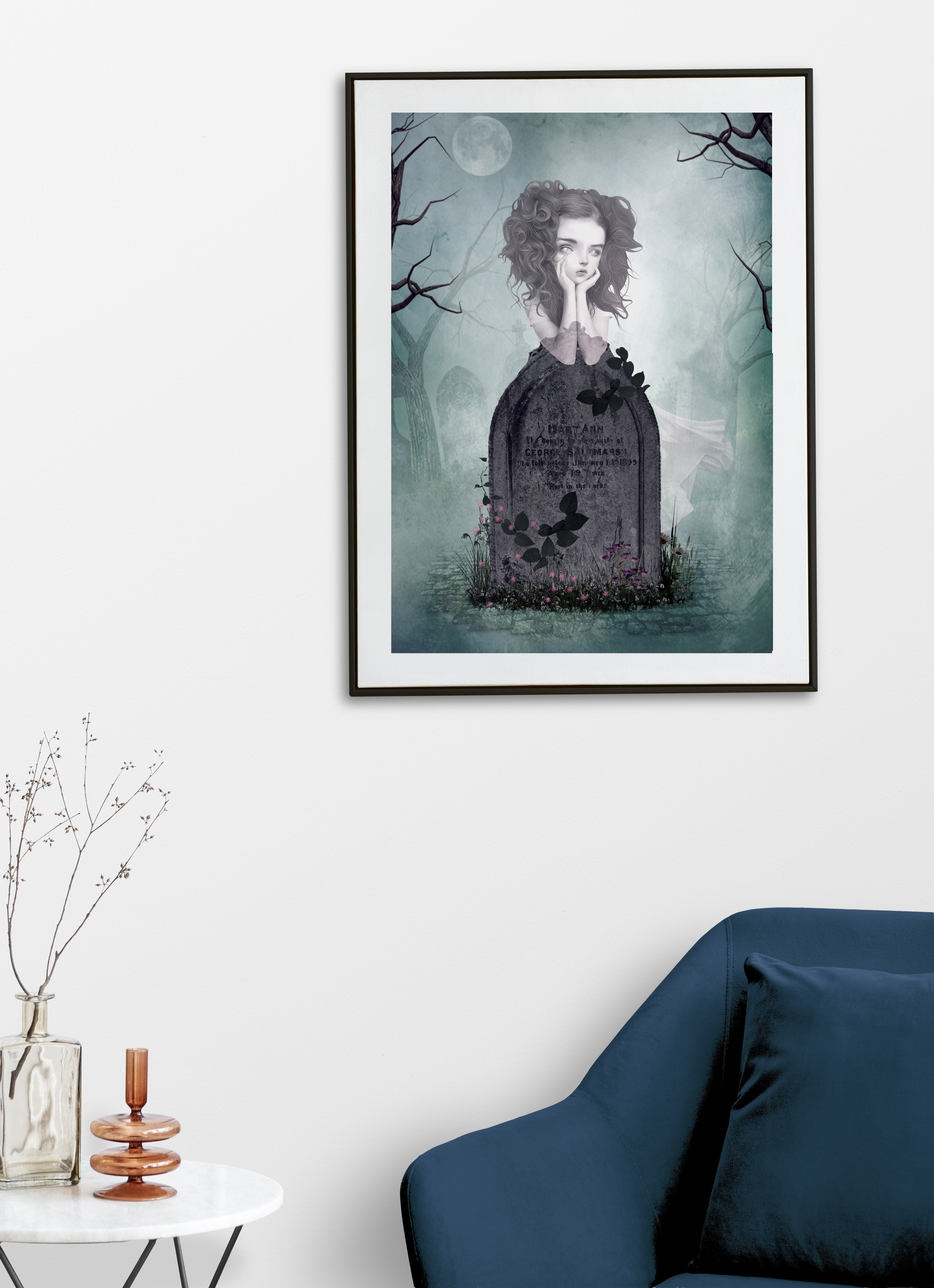 Framed artwork of a ghost girl in graveyard on a white wall above a blue sofa.
