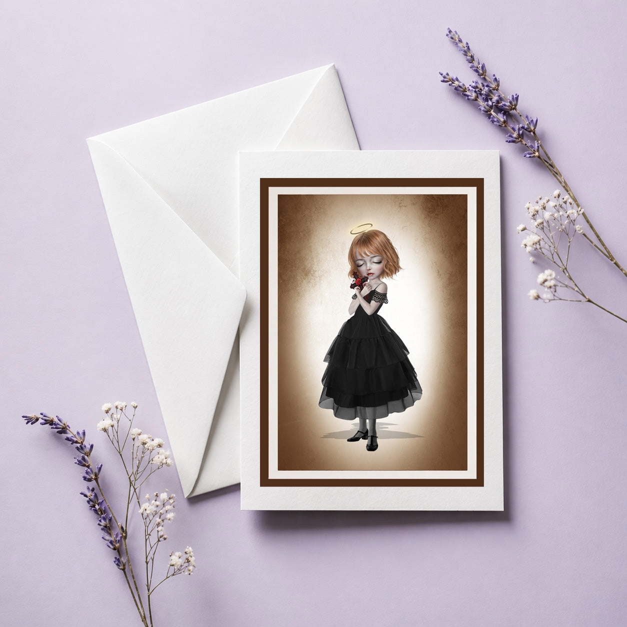 Blank gothic art greeting card with envelope featuring an angelic girl holding a crucifix, displayed with an envelope and lavender sprigs.