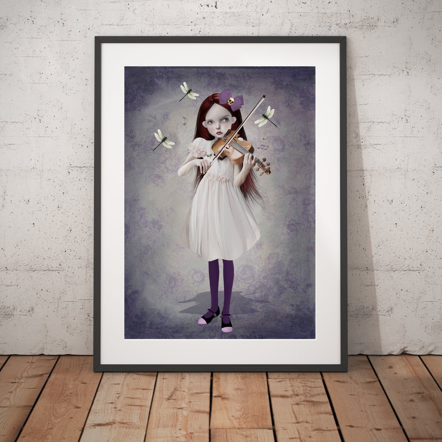 Girl and dragonflies art print in a black frame, standing against a white wall.