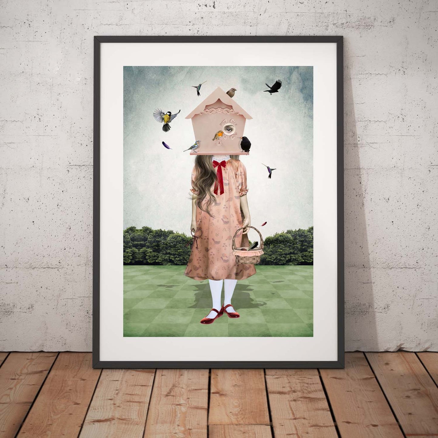 Girl and garden birds art print in a black frame, standing against a white wall.