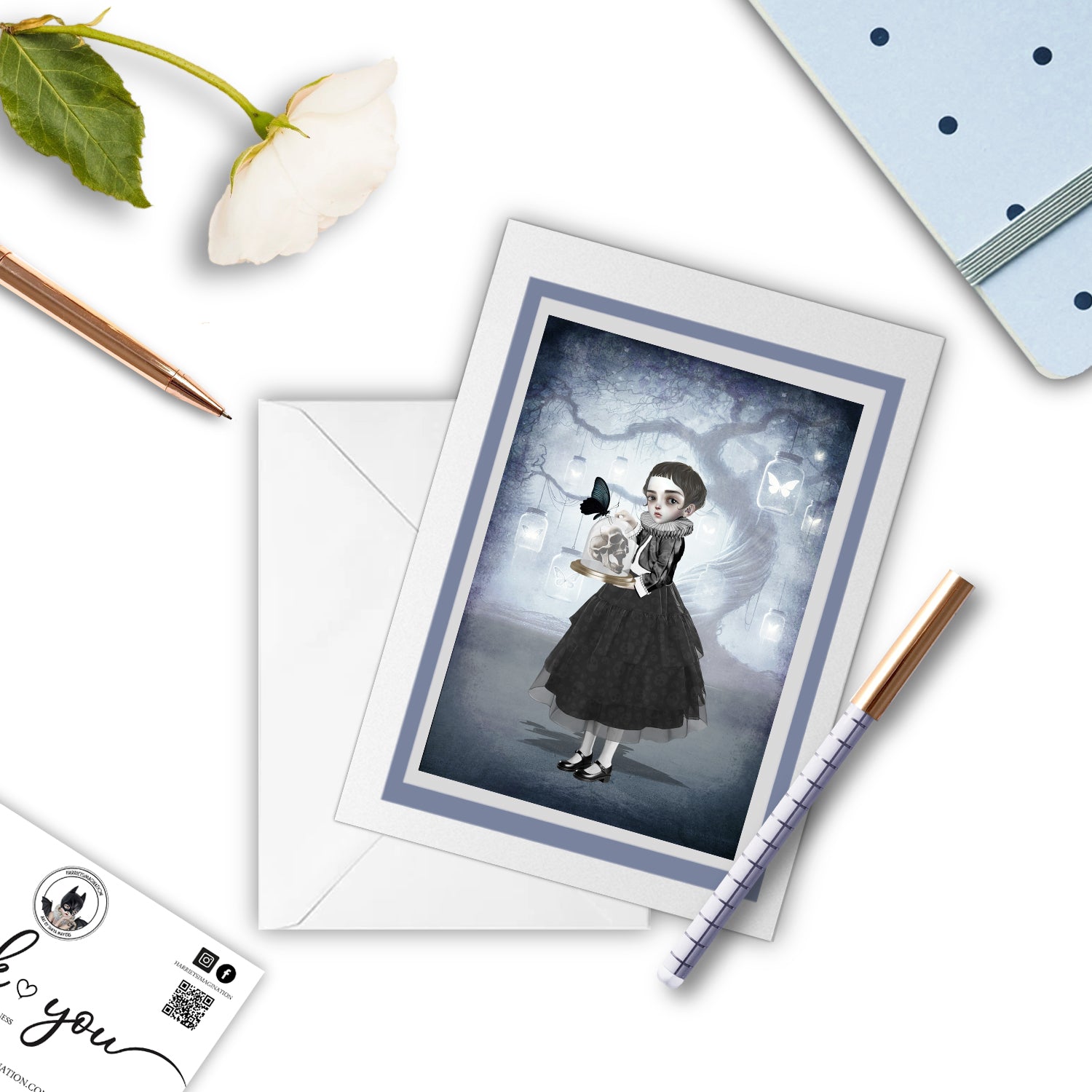 The Girl and Skull ACEO card featuring Memento Mori art, displayed alongside a notebook and pen, creating a thoughtful and artistic setup for personal notes or gifting.