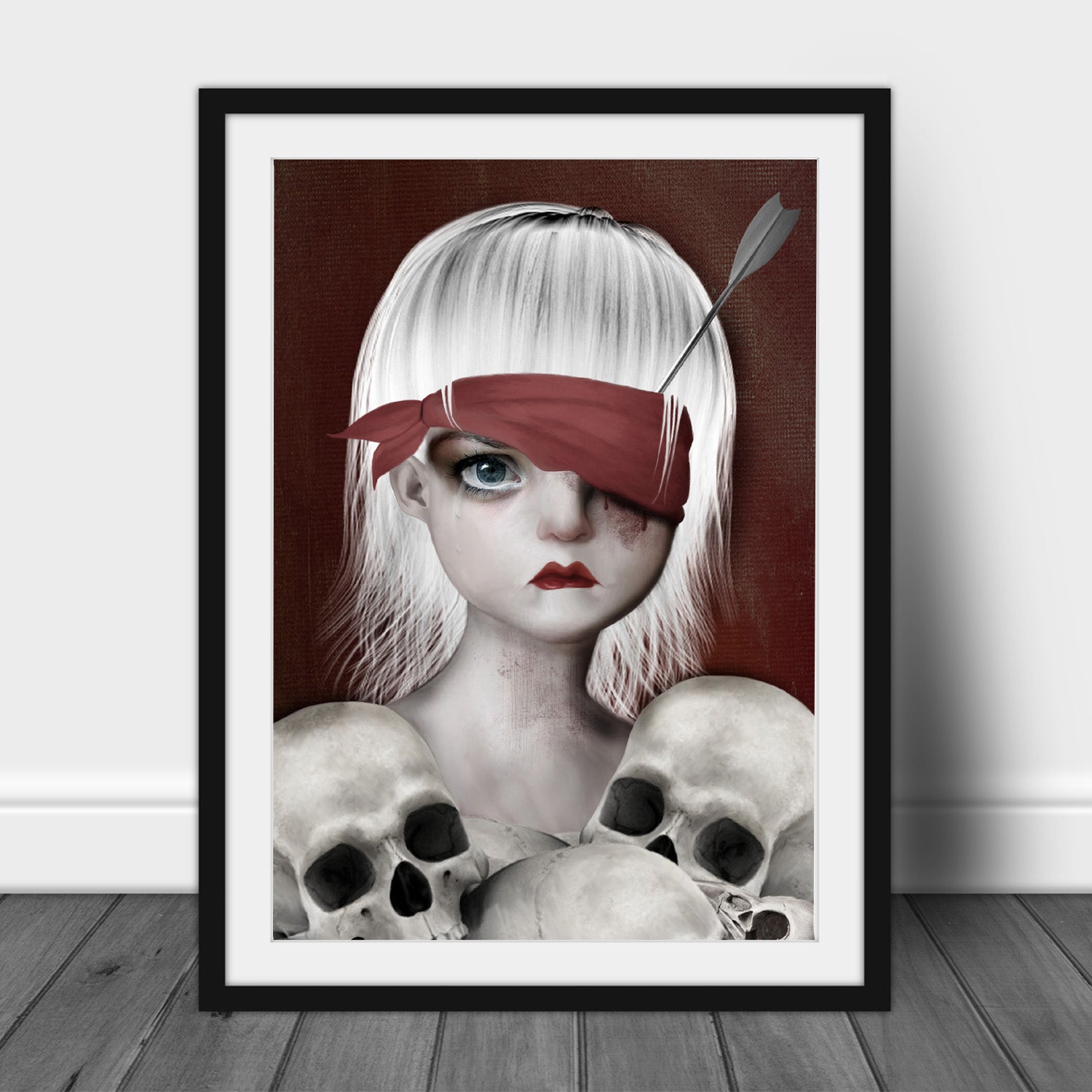 Macabre Art Print in frame. Featuring a girl with an arrow in her eye surrounded by human skulls.