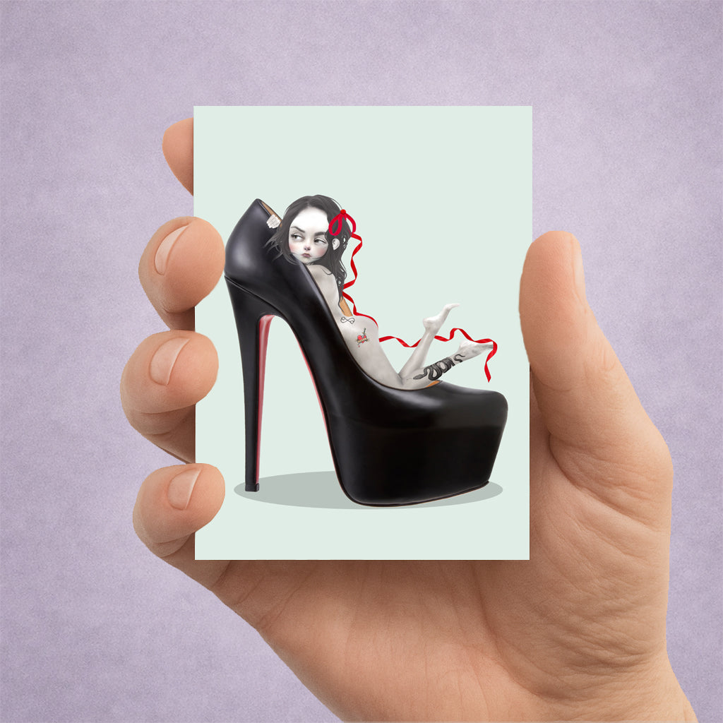 Hand holding an ACEO card with a black oversized high-heeled shoe with a girl nestled inside.