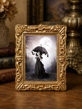 Miniature 1:12 scale gothic art print in an ornate gold frame featuring a young girl in a black Victorian dress holding an umbrella, surrounded by hanging bats beneath a full moon, displayed in a dollhouse setting.