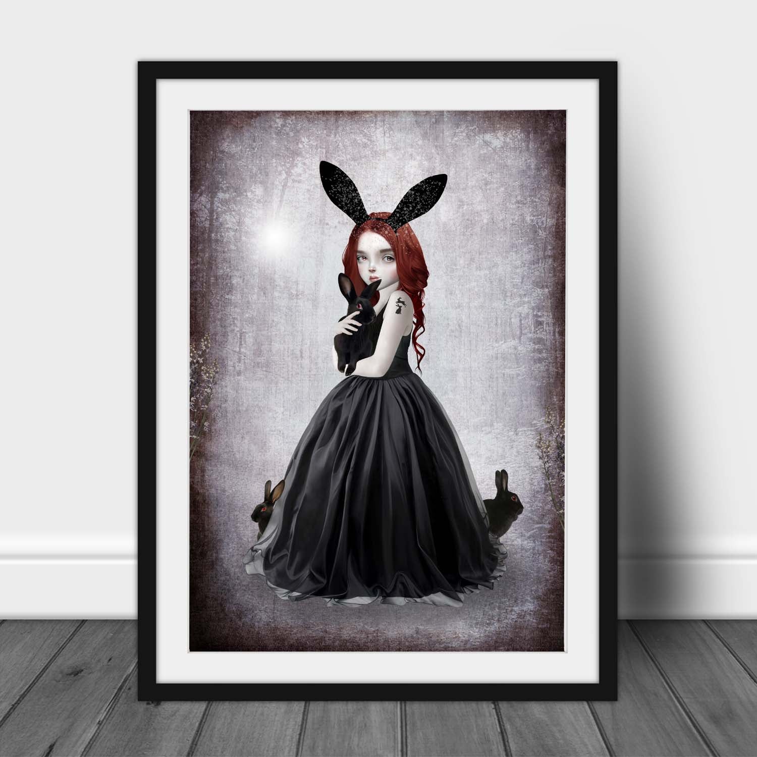 Art print of a goth girl and rabbits, in a frame, leaned against a wall.