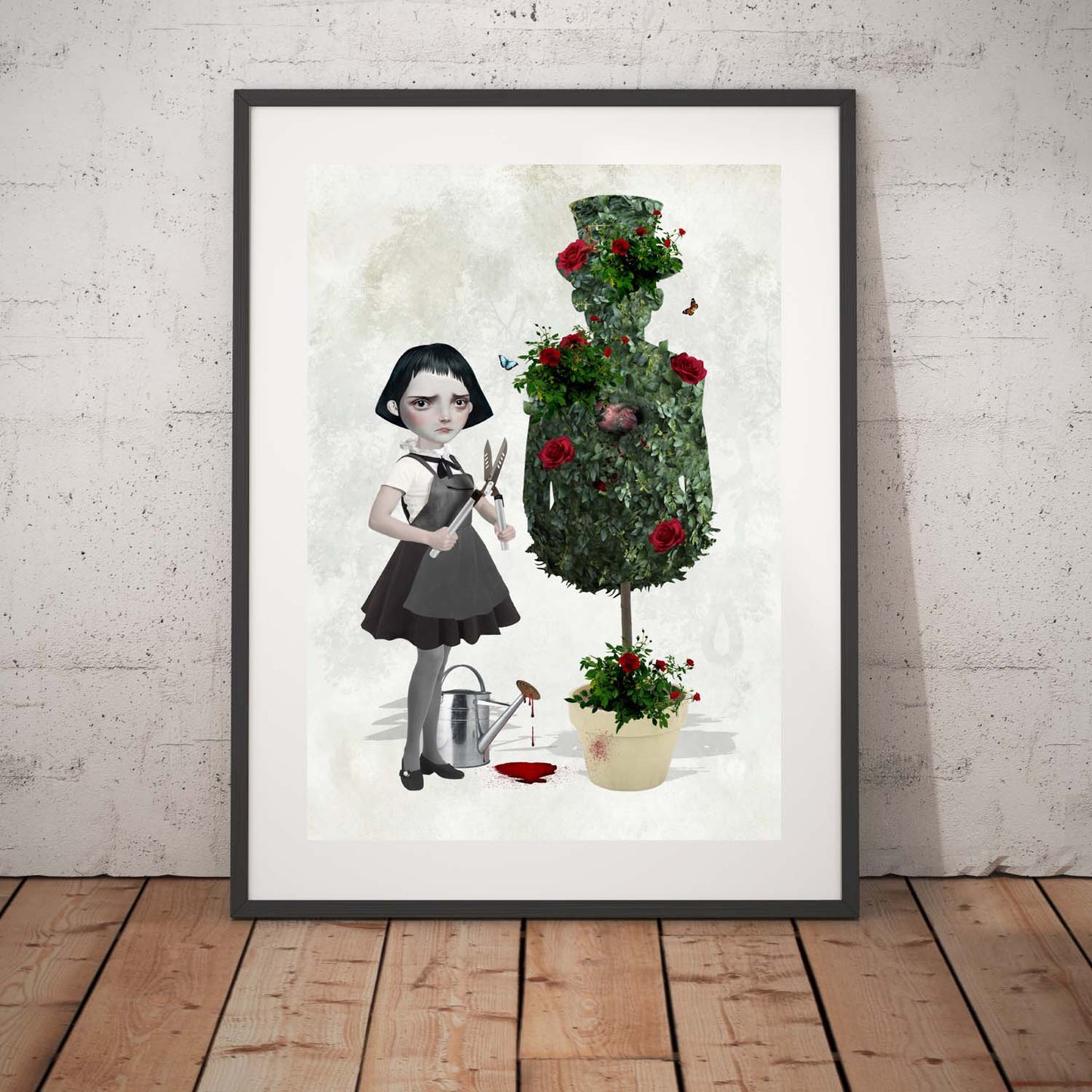 Goth Girl and topiary art print in a black frame, standing against a white wall.
