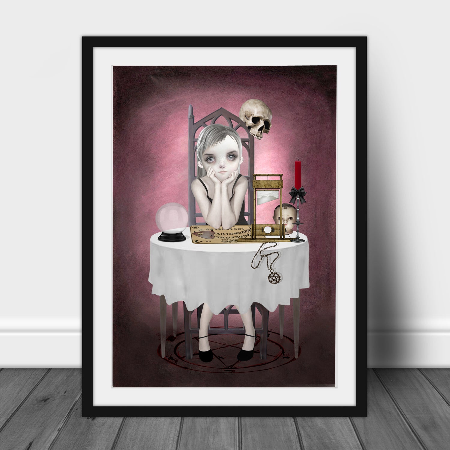 Art print of a goth girl and ouija board, in a frame, leaned against a wall.