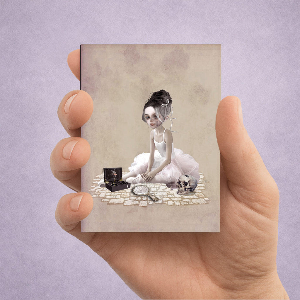 Hand holding an ACEO card with a artistic design of a gothic ballerina with a music box and skull.