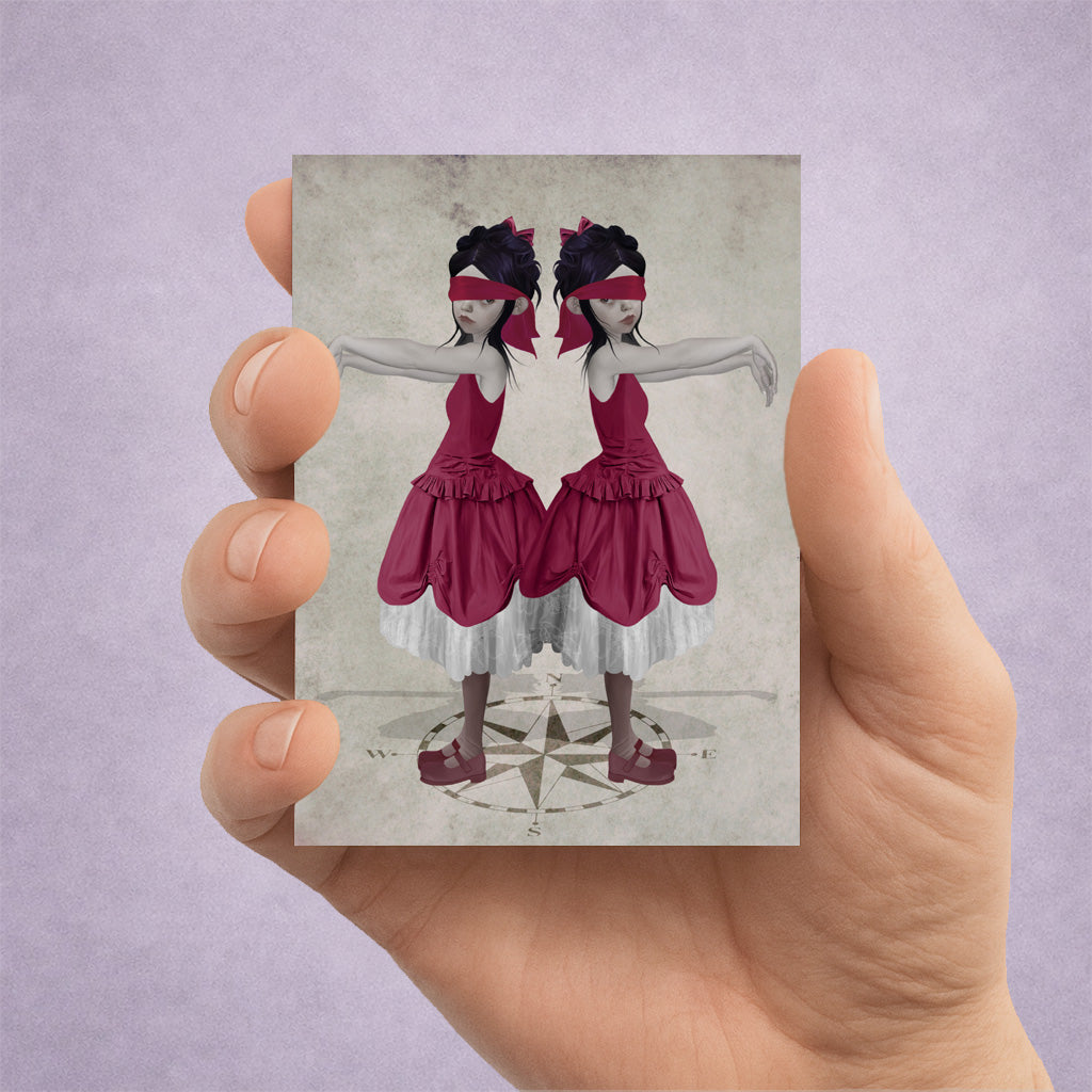 Hand holding an ACEO card with an illustration of twin girls in red dresses standing on a compass 