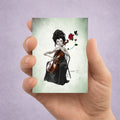 ACEO art card in hand depicting size. A dark fantasy ACEO card featuring a whimsical miniature portrait of a female cellist with a red rose and a black butterfly