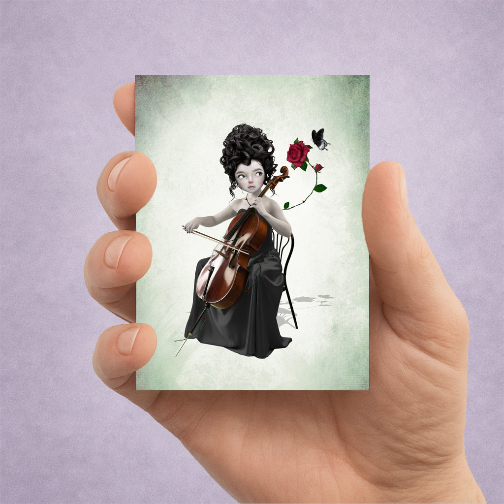 ACEO art card in hand depicting size. A dark fantasy ACEO card featuring a whimsical miniature portrait of a female cellist with a red rose and a black butterfly