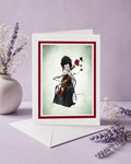 Greeting card with a woman playing a cello and holding a rose, surrounded by flowers on a light purple background.