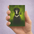 Hand holding a card with a gothic illustration of a woman against a green background surrounded by birds.