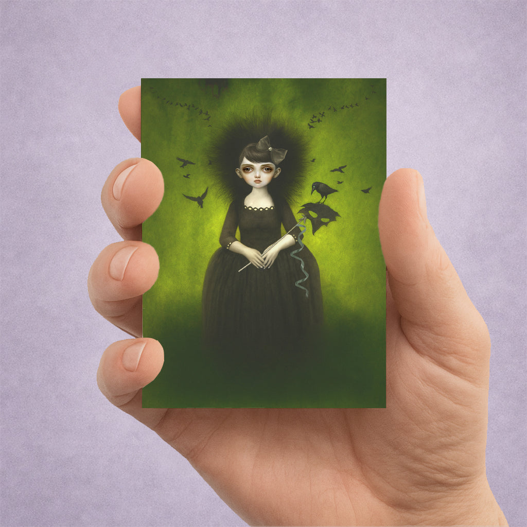 Hand holding a card with a gothic illustration of a woman against a green background surrounded by birds.