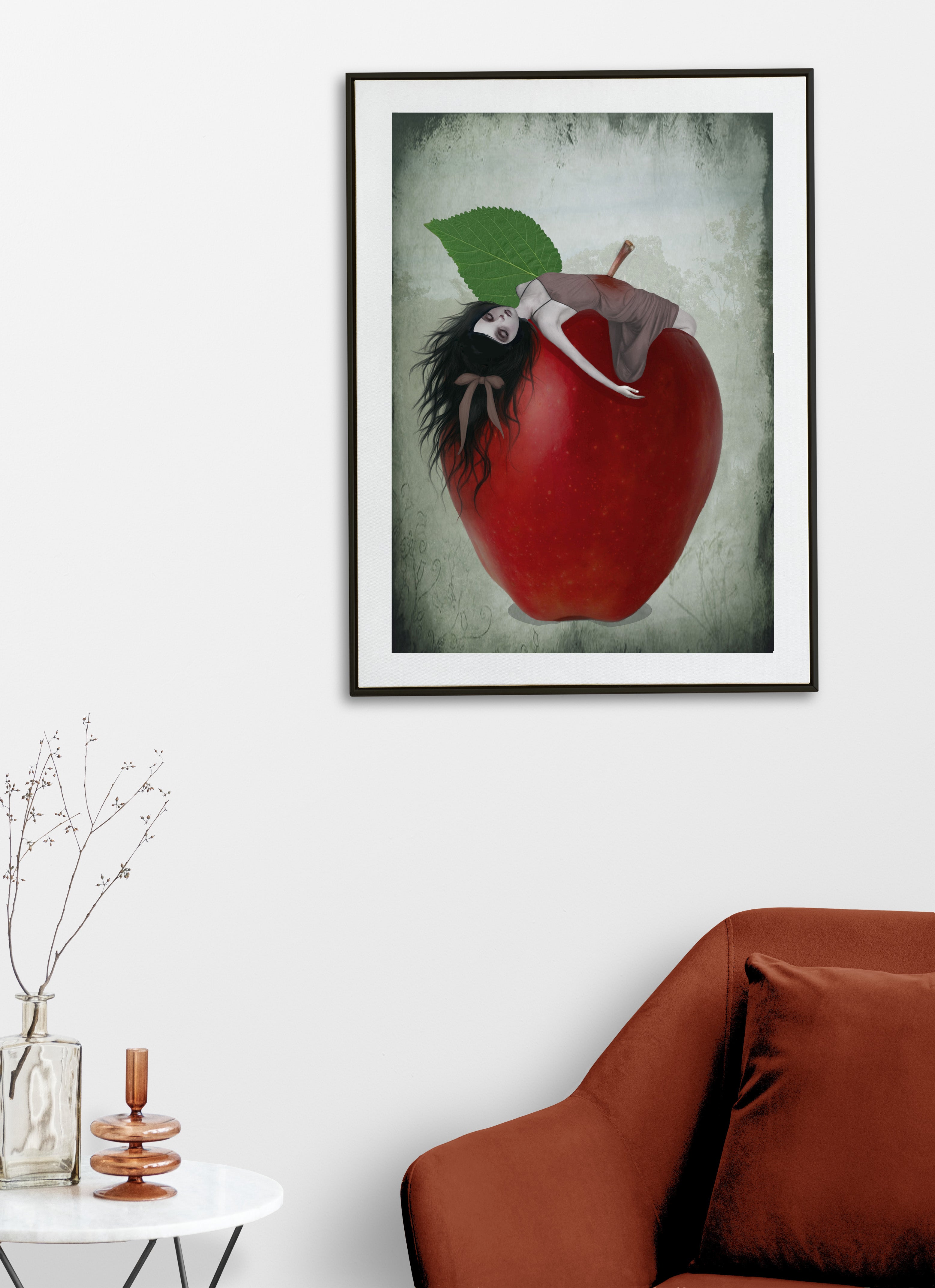 Framed gothic fairytale artwork of Snow White impaled on the stalk of a red apple on a white wall above a brown sofa.