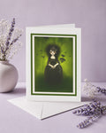Greeting card with a dark-themed illustration of a goth girl and flock of crows on a purple surface with lavender flowers.