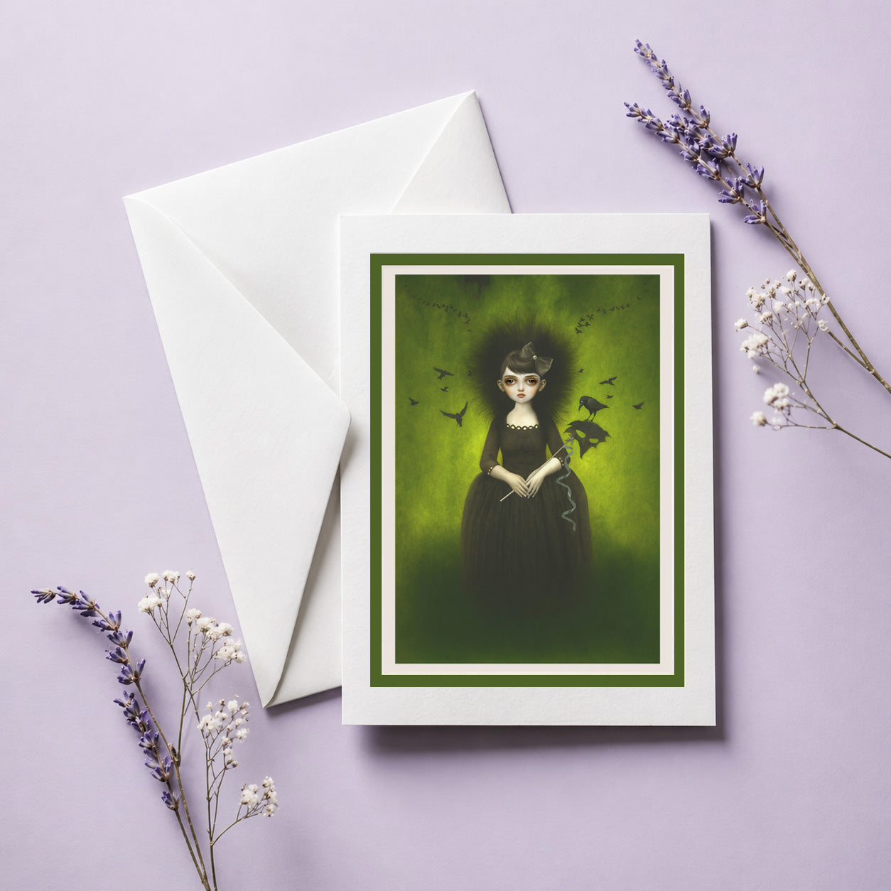Greeting card with a dark-themed illustration of a girl in a black dress surrounded by birds on a purple background, accompanied by a white envelope and dried flowers.