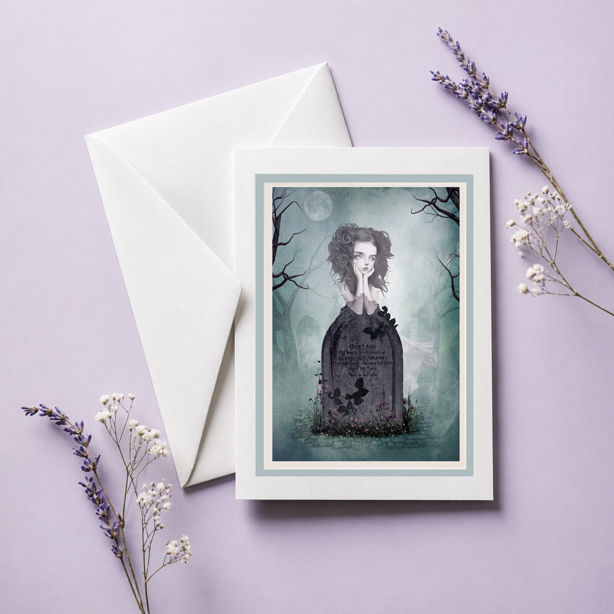 Greeting card with a ghost girl resting on her  gravestone, envelope, and lavender flowers on a light purple background